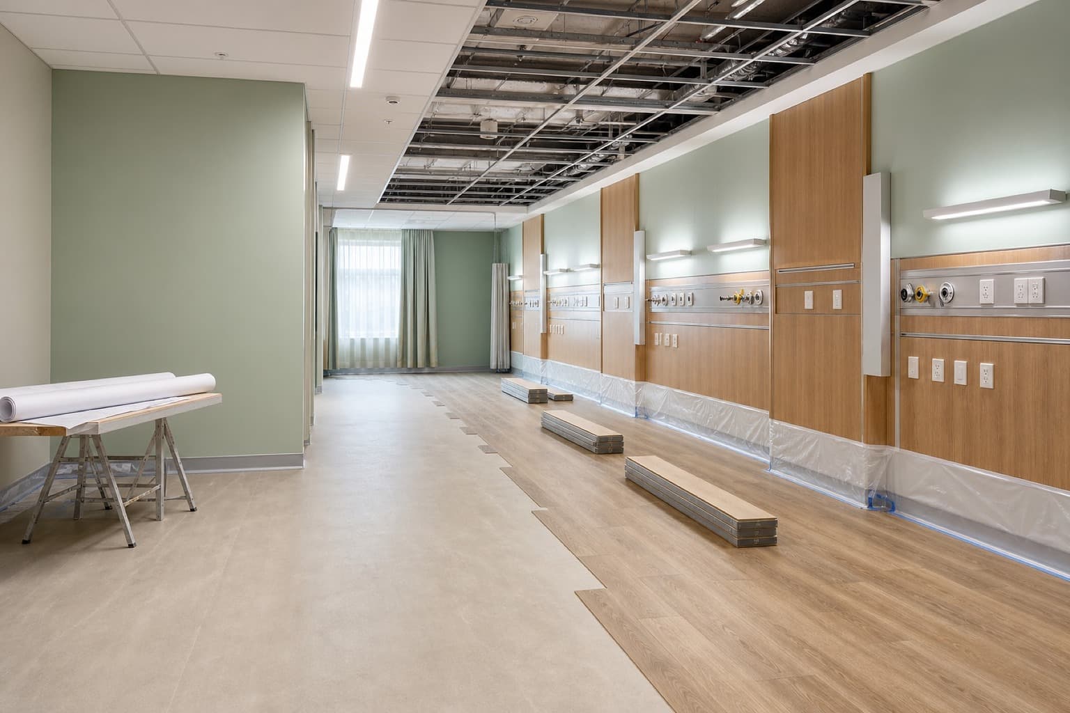 A hospital ward mid-fit-out, ceiling grid part-tiled and headwall panelling installed